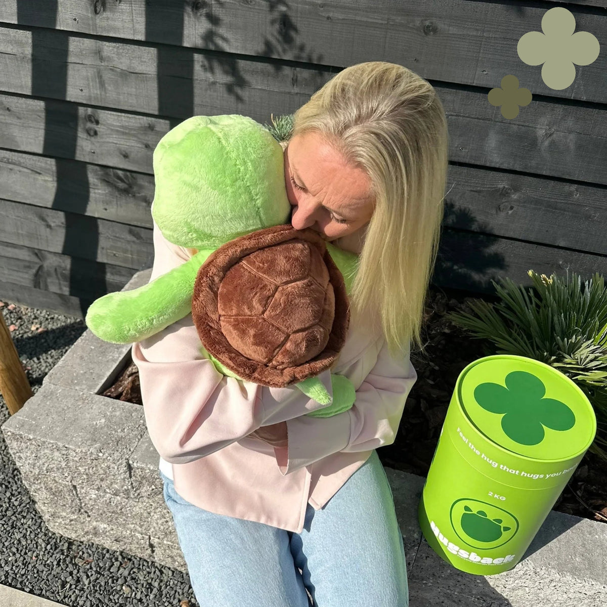 Vrouw in de tuin knuffelt de Hugsback Schildpad naast de groene cadeaukoker