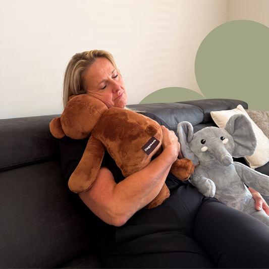 Vrouw ontspant met Hugsback verzwaarde knuffelbeer en knuffelolifant voor rust en comfort op de bank