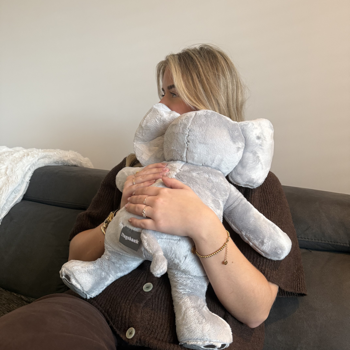 Vrouw houdt de grijze Hugsback verzwaringsknuffel olifant tegen zich aan op de bank