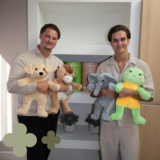 Timo et Noah de Hugsback côte à côte avec les peluches lestées devant une étagère de tubes cadeaux Hugsback