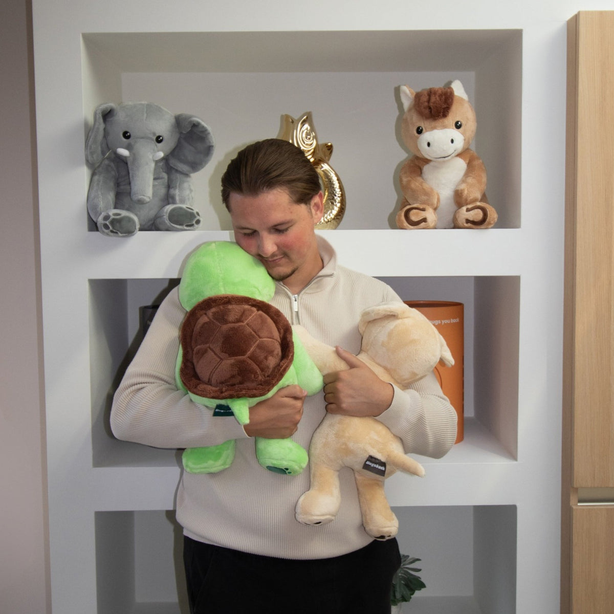 Woman holding the green Hugsback weighted plush turtle in front of a shelf with gift tubes