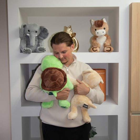 Femme tenant la peluche lestée tortue Hugsback verte dans ses bras devant une étagère avec des tubes cadeaux