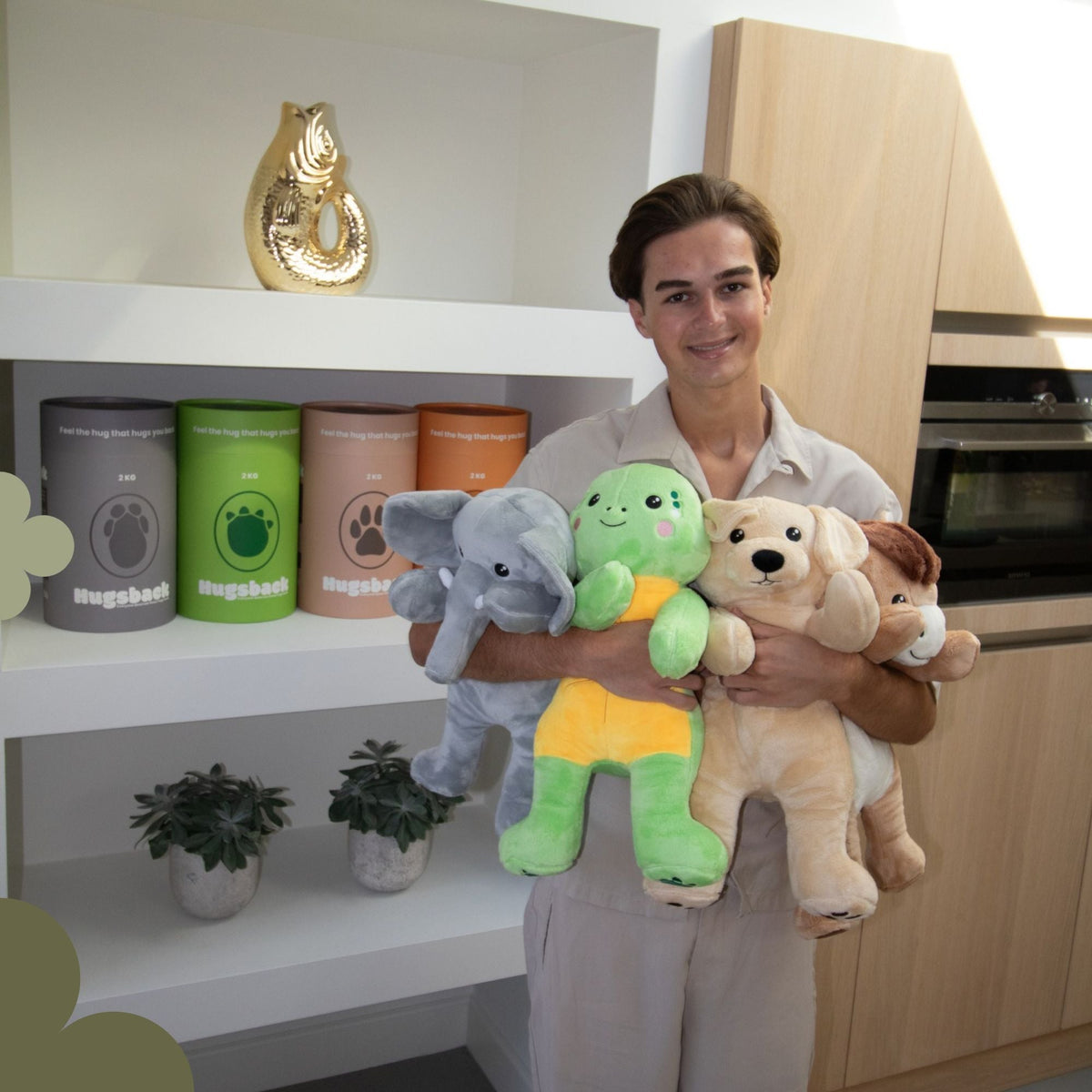 Jeune homme portant l'éléphant, la tortue, le chien et le cheval Hugsback dans ses bras devant une étagère de tubes cadeaux