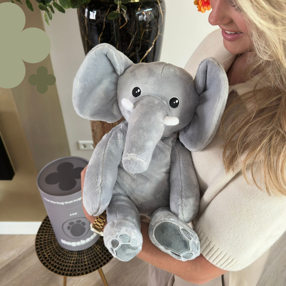 Vrouw houdt de grijze Hugsback verzwaringsknuffel olifant vast naast de grijze cadeaukoker