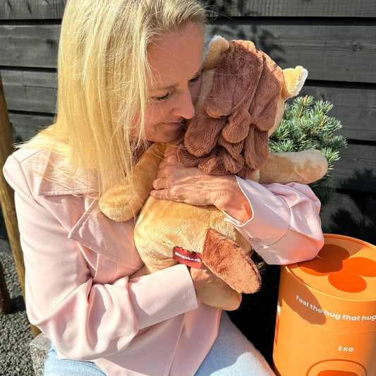 Femme serrant fort la peluche lestée cheval Hugsback marron dans ses bras dans le jardin à côté du tube cadeau orange