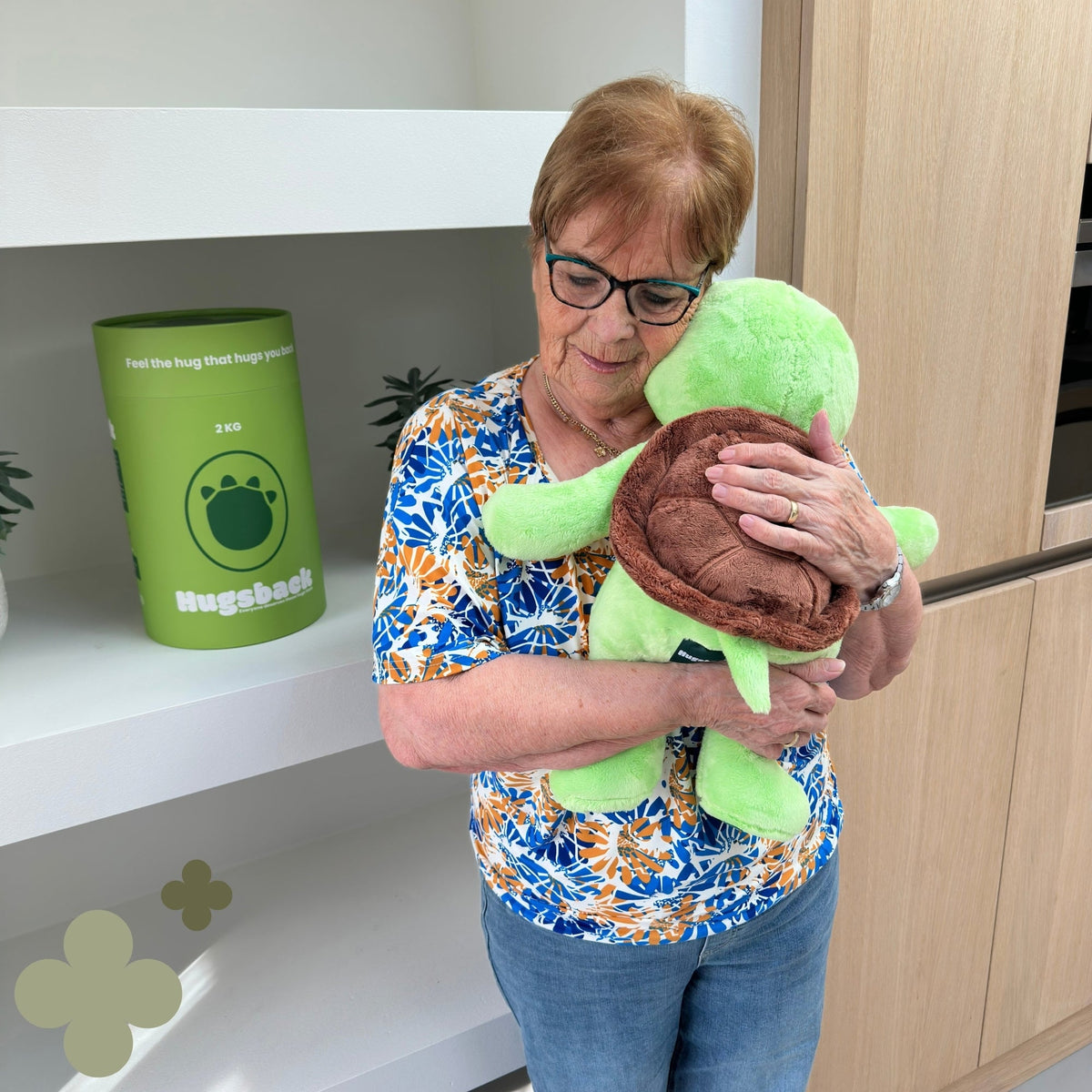 Oudere vrouw knuffelt de groene Hugsback Schildpad bij de groene cadeaukoker