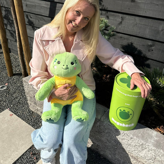 Woman with the green Hugsback weighted plush turtle in the garden next to the green gift tube