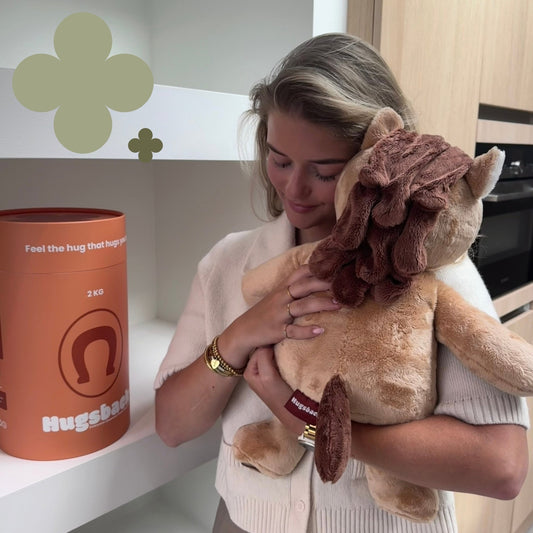 Jonge vrouw knuffelt de bruine Hugsback verzwaringsknuffel paard naast de oranje cadeaukoker
