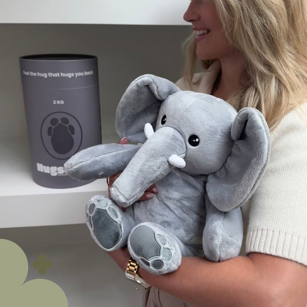 Person holding the grey Hugsback weighted plush elephant next to the grey gift tube