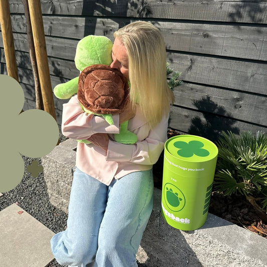 Vrouw knuffelt de groene Hugsback verzwaringsknuffel schildpad in de tuin naast de groene cadeaukoker