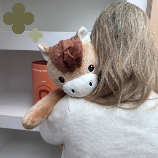 Woman hugging the brown Hugsback weighted plush horse over her shoulder seen from behind