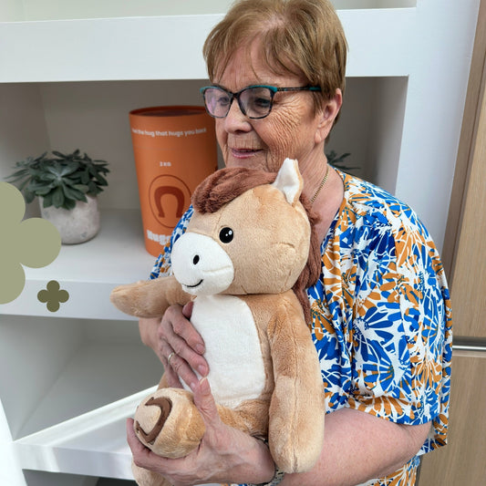 Older woman holding the brown Hugsback weighted plush horse next to the orange gift tube