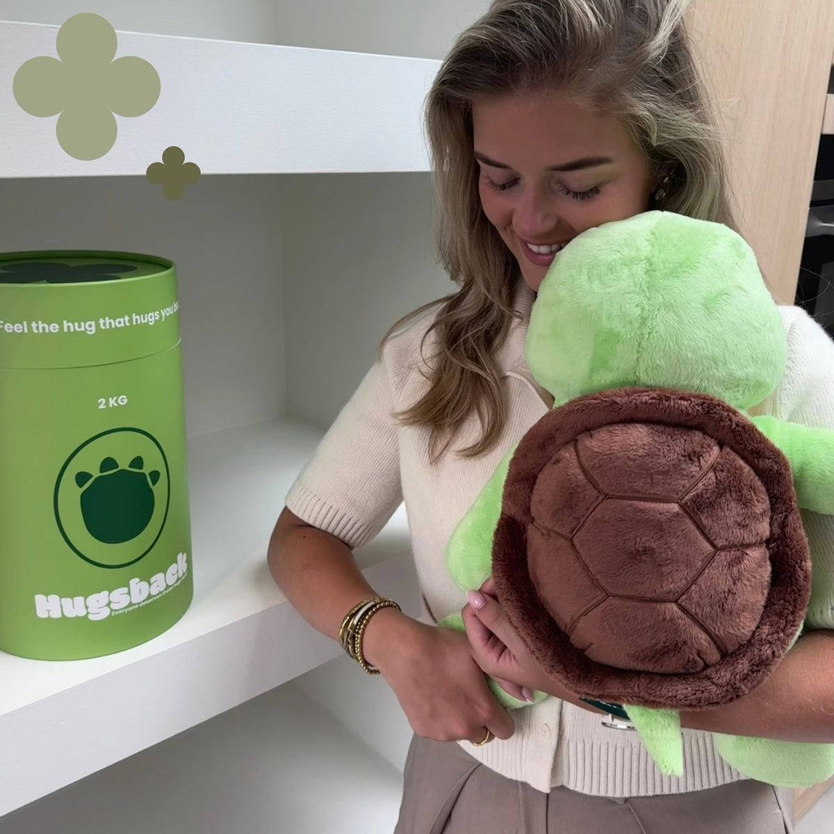 Jeune femme serrant la peluche lestée tortue Hugsback verte dans ses bras à côté du tube cadeau vert