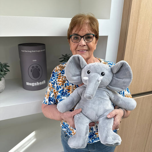 Oudere vrouw met de grijze Hugsback verzwaringsknuffel olifant naast de grijze cadeaukoker