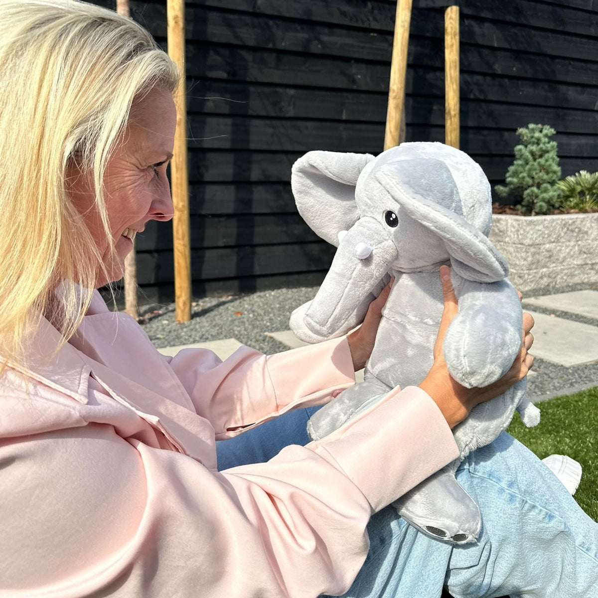 Vrouw houdt de grijze Hugsback verzwaringsknuffel olifant omhoog in de tuin