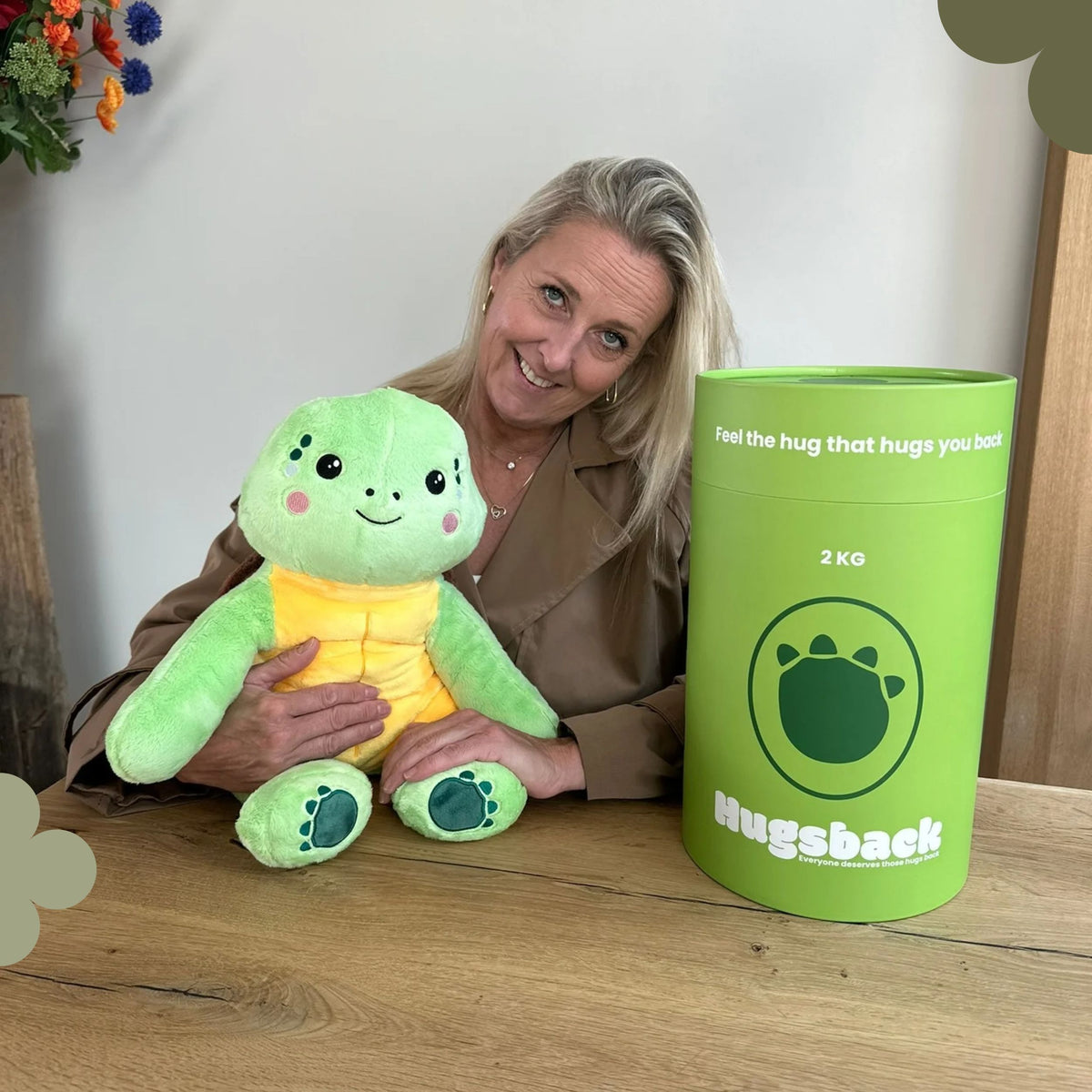Vrouw aan tafel met de groene verzwaringsknuffel schildpad naast de groene Hugsback cadeaukoker