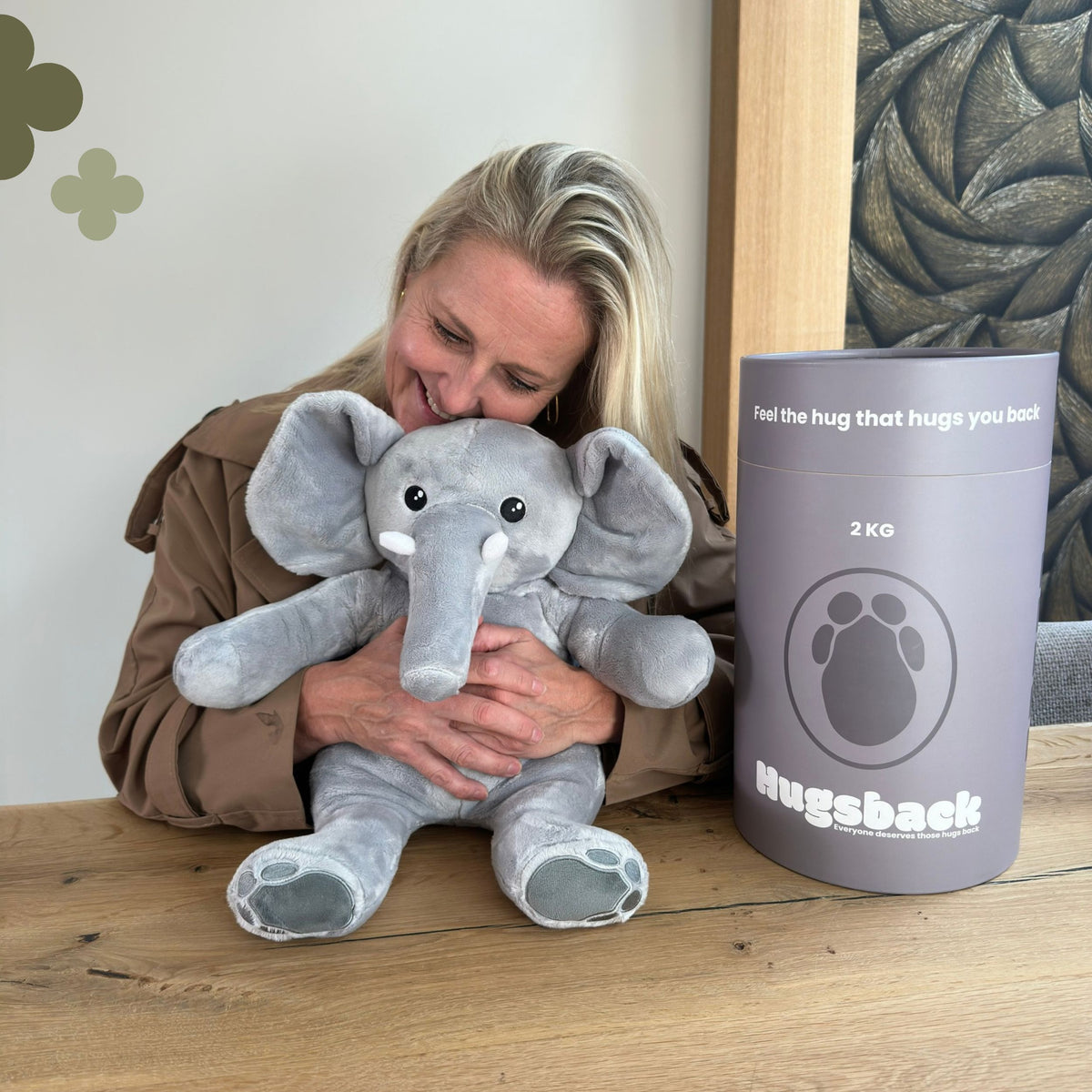 Kvinde ved et bord, der krammer den grå tyngdebamse elefant ved siden af Hugsbacks grå gaverør