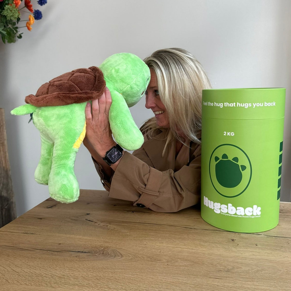 Vrouw die de groene verzwaringsknuffel schildpad knuffelt naast de groene Hugsback cadeaukoker