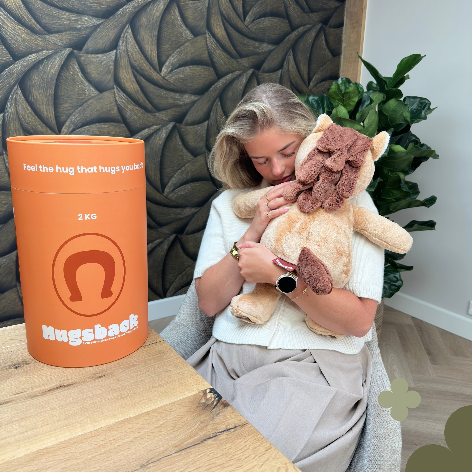 Vrouw die de bruine verzwaringsknuffel paard knuffelt naast de oranje Hugsback cadeaukoker