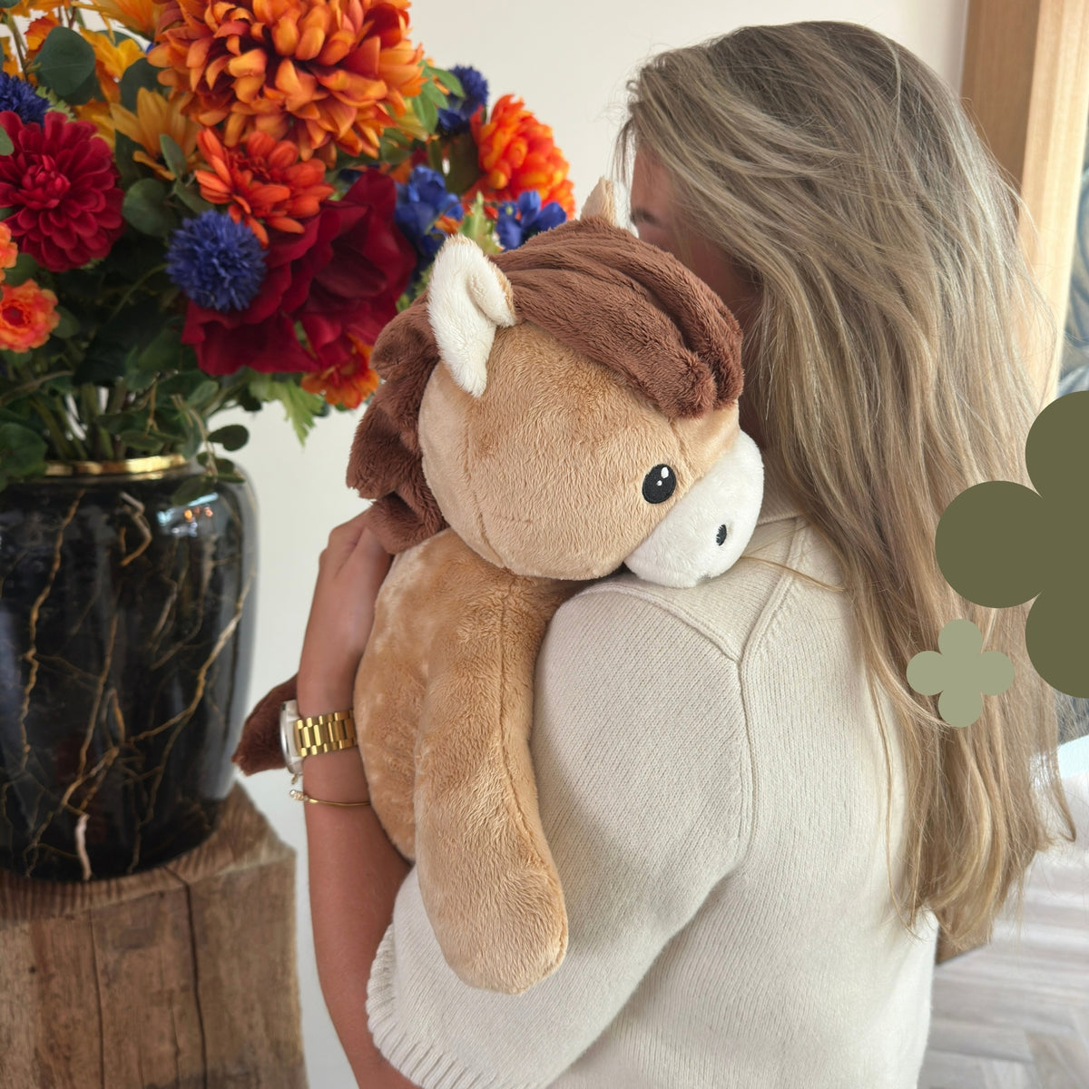 Femme avec la peluche lestée cheval marron sur l'épaule près d'un bouquet de fleurs