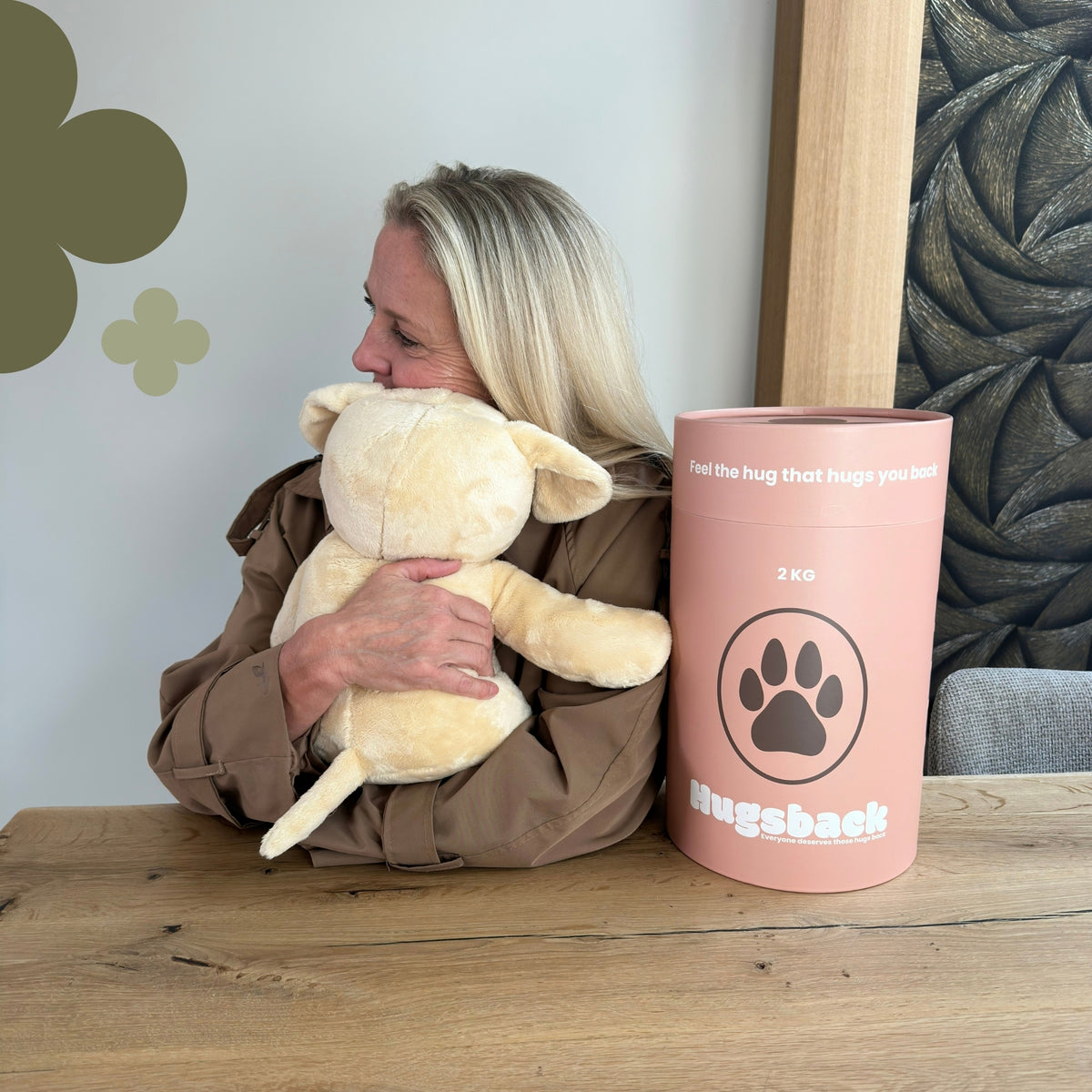 Frau am Tisch, die das beige Gewichtskuscheltier Hund neben der rosa Hugsback-Geschenkröhre knuddelt
