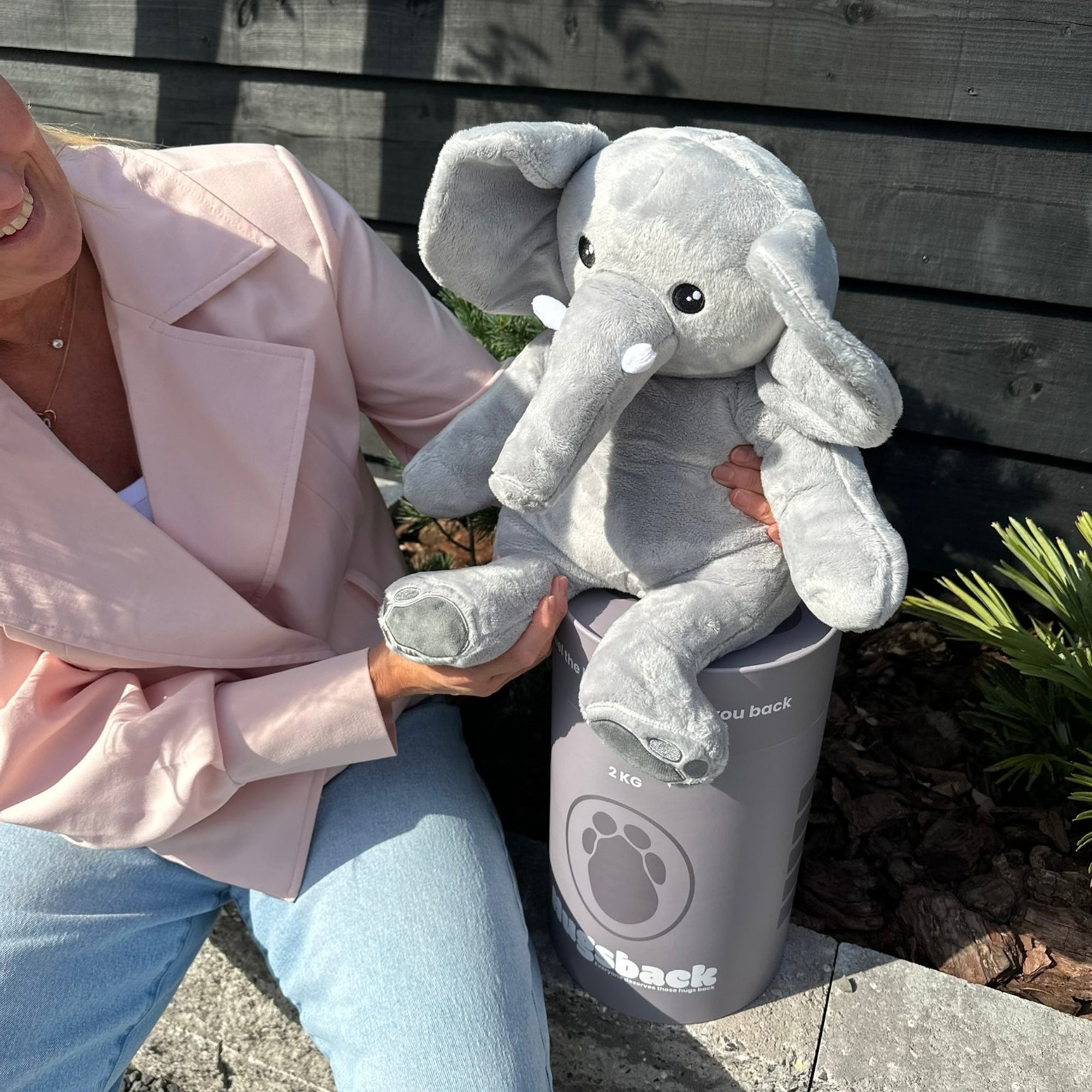 Vrouw die buiten de grijze verzwaringsknuffel olifant op de grijze Hugsback cadeaukoker zet