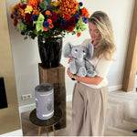 Frau mit dem grauen Gewichtskuscheltier Elefant bei einem Blumenstrauß und der grauen Geschenkröhre