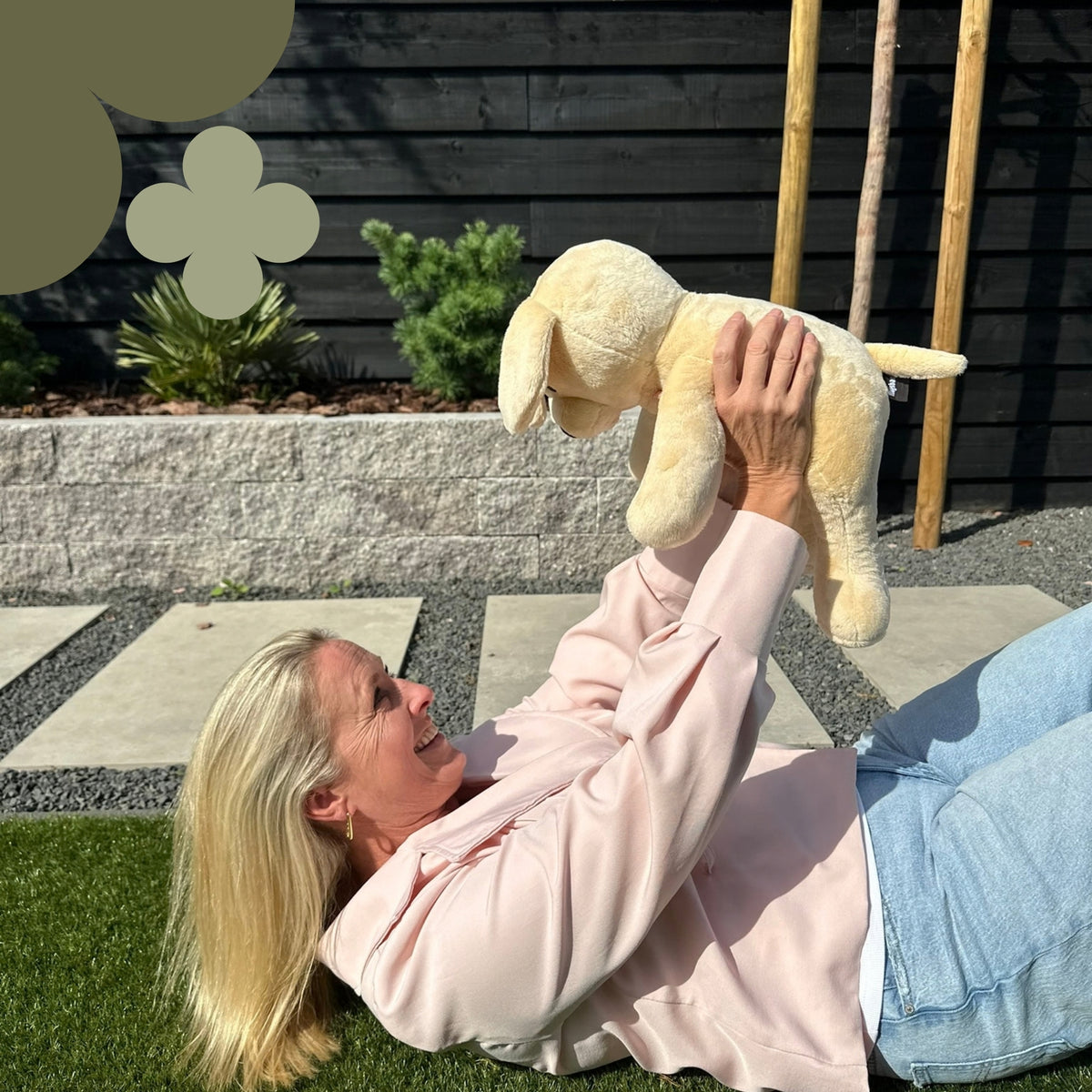 Femme allongée dans l'herbe qui soulève la peluche lestée chien beige