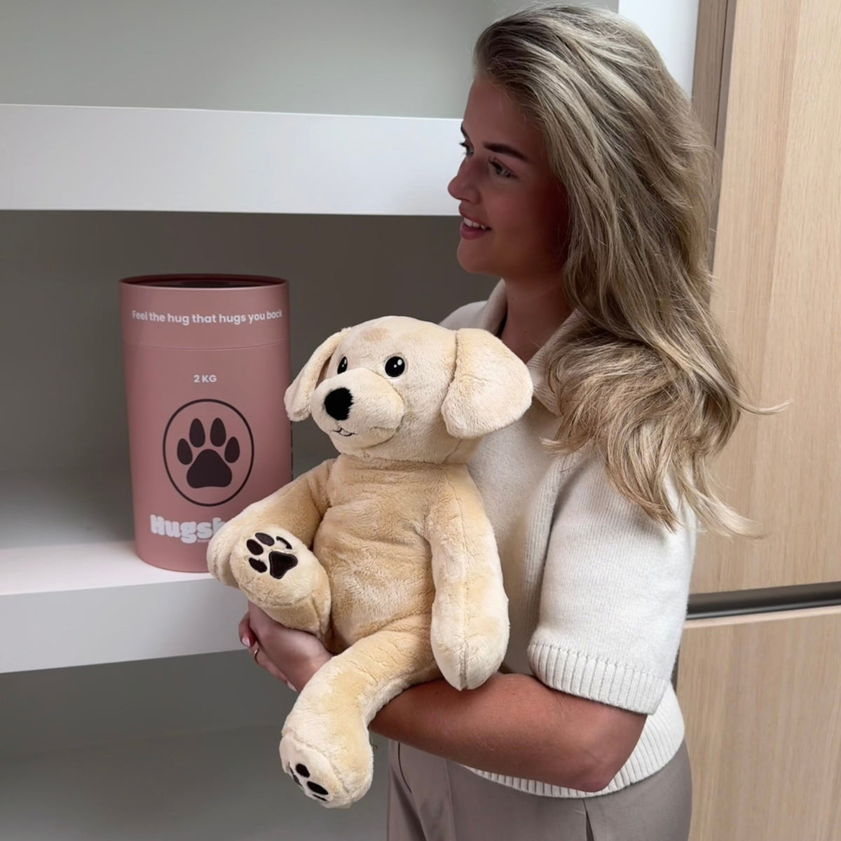 Junge Frau mit dem beigen Gewichtskuscheltier Hund bei der rosa Hugsback-Geschenkröhre