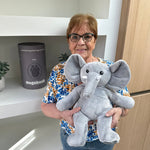 Femme âgée avec la peluche lestée éléphant grise devant un placard avec le tube cadeau gris