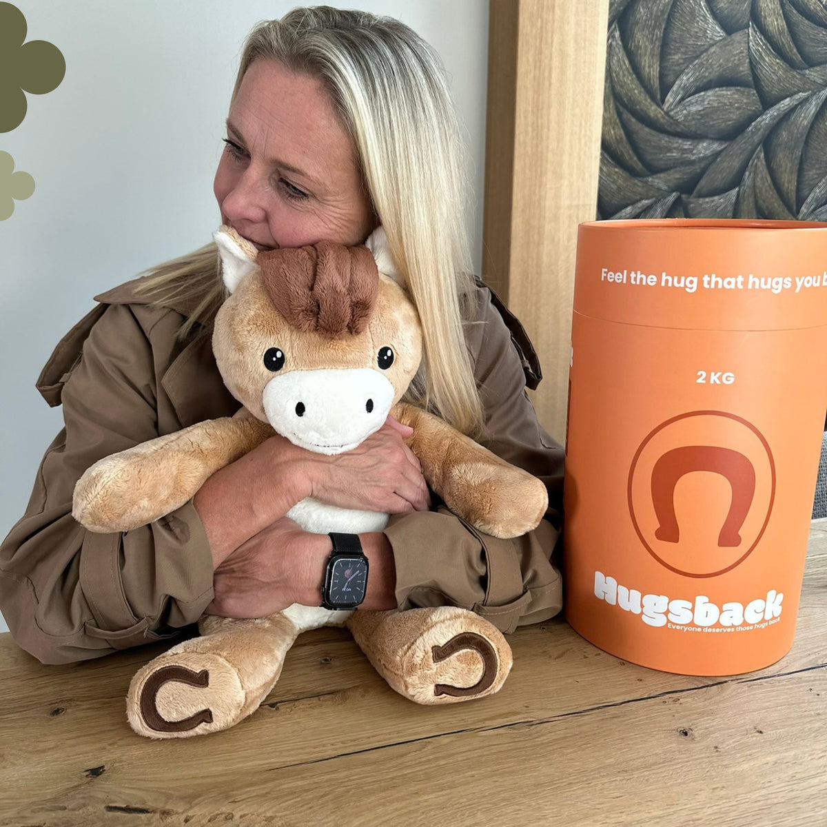 Kvinde ved et bord, der krammer den brune tyngdebamse hest ved siden af Hugsbacks orange gaverør