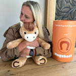 Kvinde ved et bord, der krammer den brune tyngdebamse hest ved siden af Hugsbacks orange gaverør