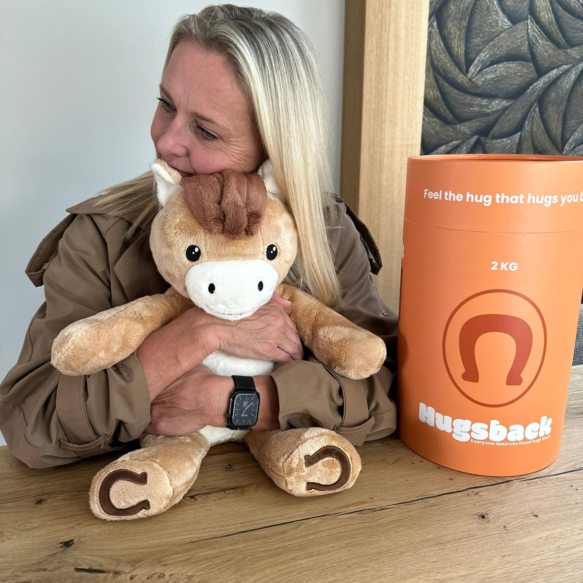 Kvinde ved et bord, der krammer den brune tyngdebamse hest ved siden af Hugsbacks orange gaverør