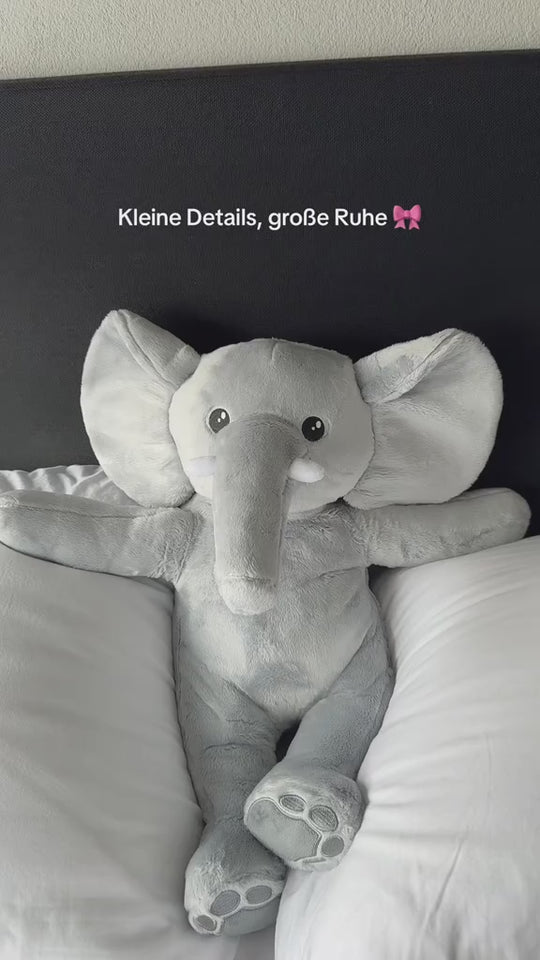 Duitstalige video van de grijze verzwaringsknuffel olifant op een wit bed, met de tekst: kleine details, grote rust